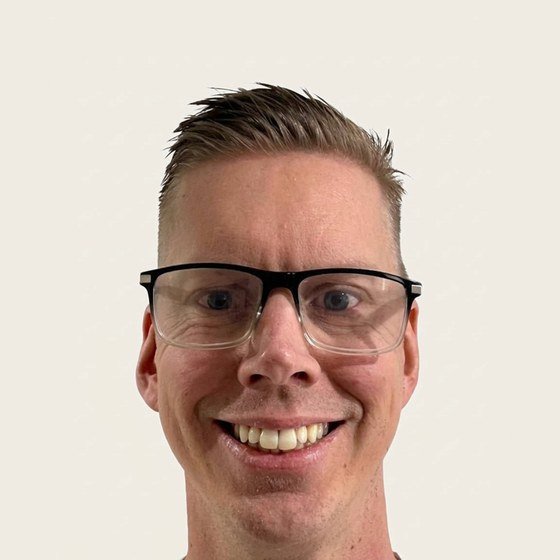 Joel Perkes, who writes Debasement Basement: a smiling man in his forties with short fair hair and black-rimmed glasses, photographed against a plain backdrop.
